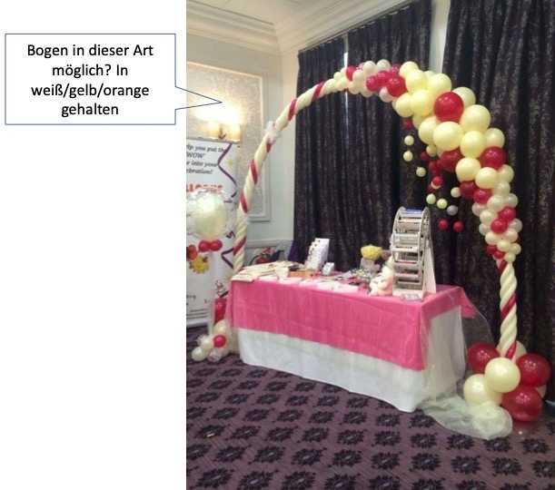 Ein Ballonbogen über einem Tisch mit einer Tischdecke, rosa Tisch und zwei Ballons mit Schleifen.